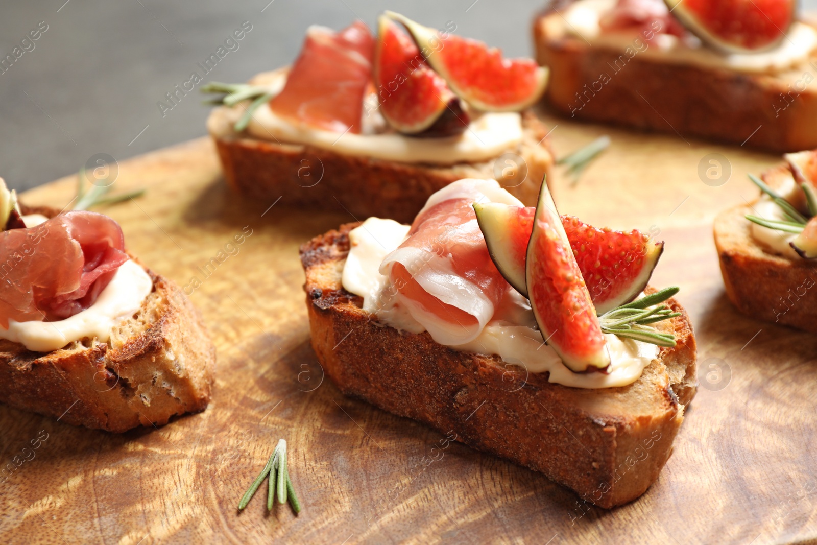 Photo of Bruschettas with cream cheese, prosciutto and figs served on wooden board, closeup