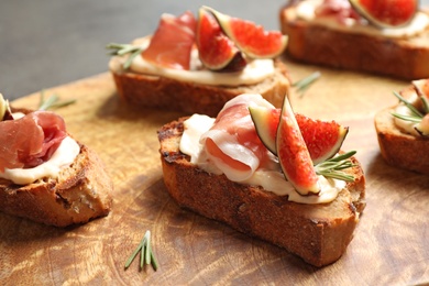 Photo of Bruschettas with cream cheese, prosciutto and figs served on wooden board, closeup