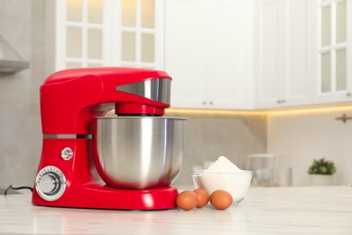 Modern red stand mixer, eggs and bowl with flour on white marble table in kitchen, space for text