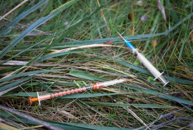 Photo of Disposable syringes with needles on green grass outdoors