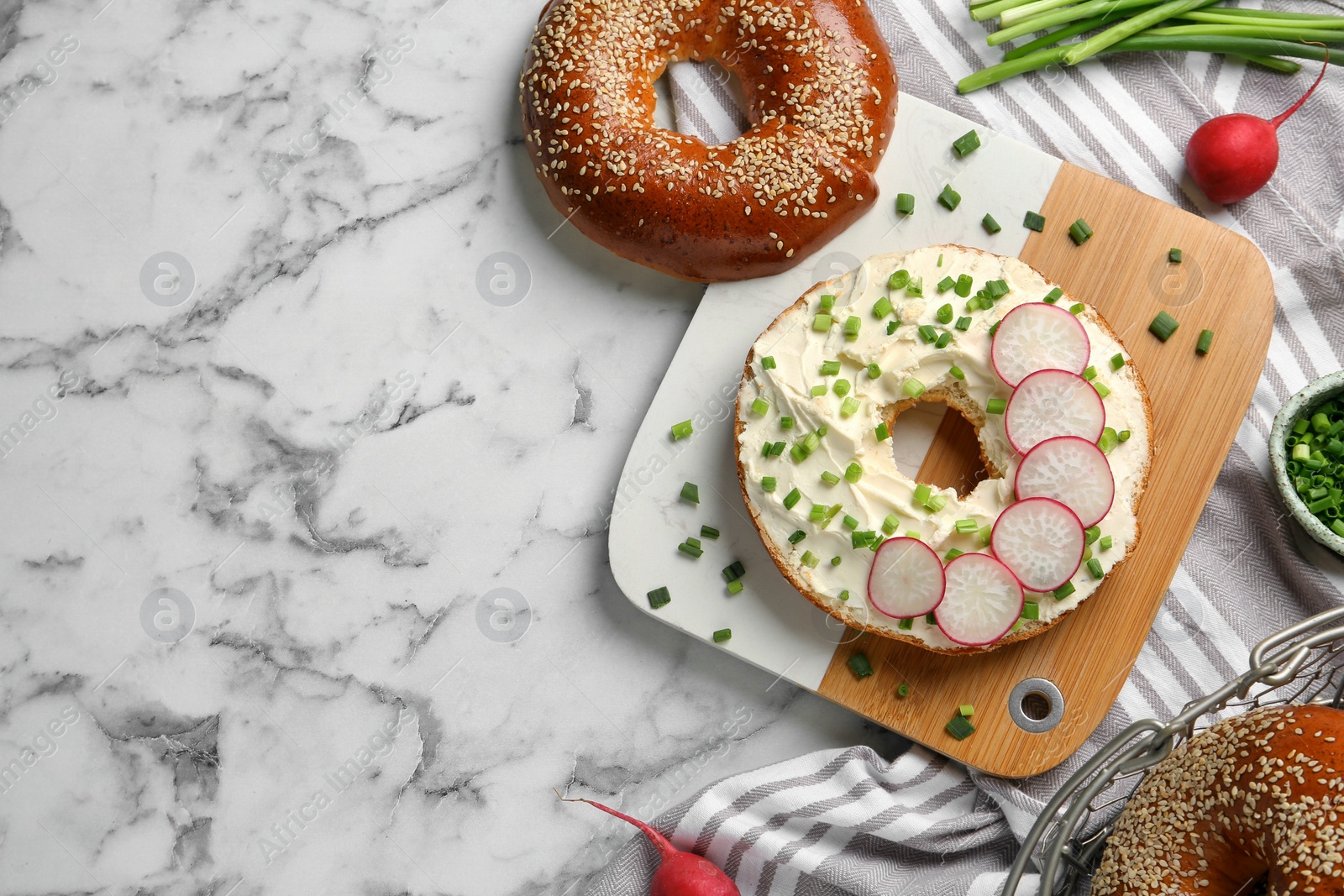 Photo of Delicious bagel with cream cheese, green onion and radish on white marble table, flat lay. Space for text