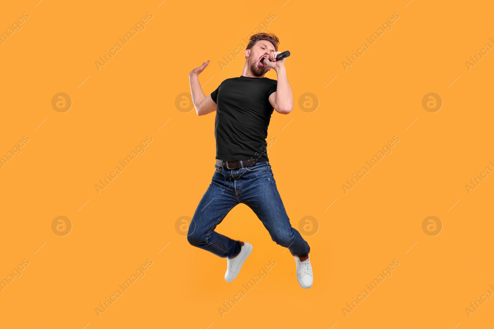 Photo of Handsome man with microphone singing and jumping on yellow background