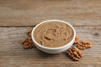 Photo of Delicious nut butter in bowl and walnuts on wooden table, closeup