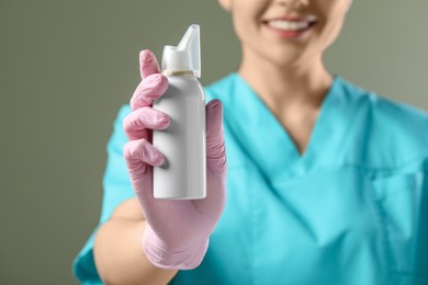 Photo of Woman holding nasal spray bottle on olive background, closeup