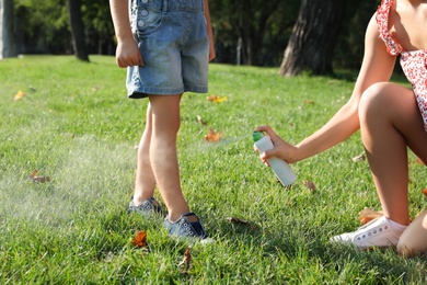 Photo of Mother applying insect repellent onto girl's leg in park, closeup