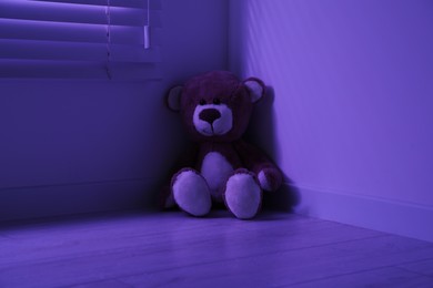 Photo of Cute lonely teddy bear on floor in corner of dark room