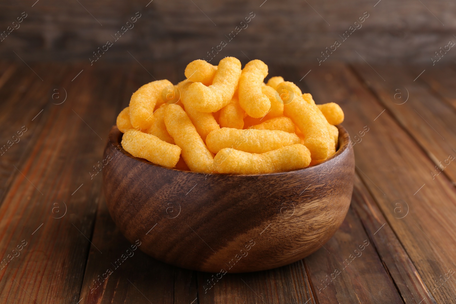 Photo of Bowl of tasty cheesy corn puffs on wooden table