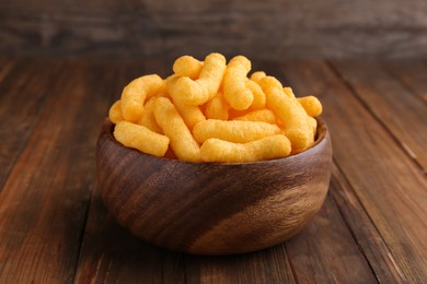 Photo of Bowl of tasty cheesy corn puffs on wooden table