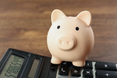 Calculator and piggy bank on wooden table, closeup