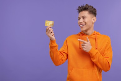 Photo of Happy man pointing at credit card on purple background. Space for text