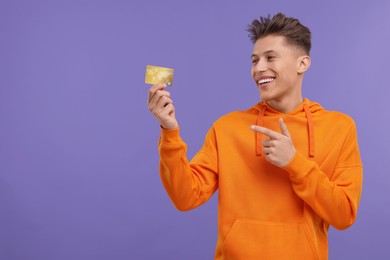 Happy man pointing at credit card on purple background. Space for text