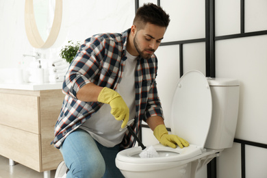 Young man cleaning toilet bowl in bathroom