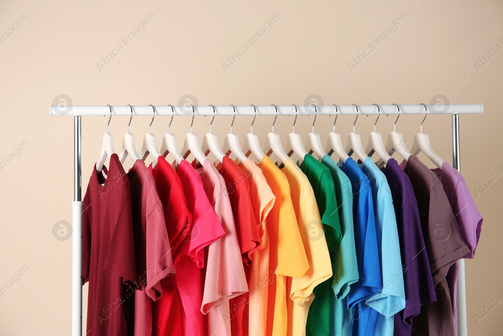 Photo of Many t-shirts hanging in order of rainbow colors on light background