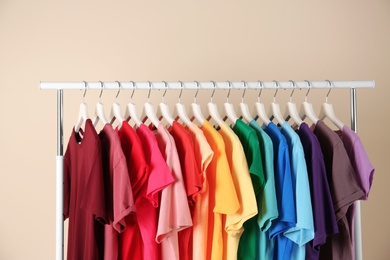 Photo of Many t-shirts hanging in order of rainbow colors on light background