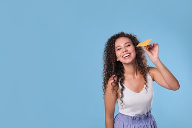 Photo of Beautiful African-American woman playing with paper plane on light blue background. Space for text