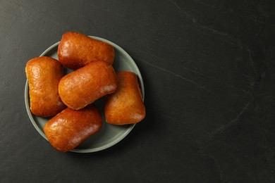 Photo of Delicious baked pirozhki on black table, top view. Space for text