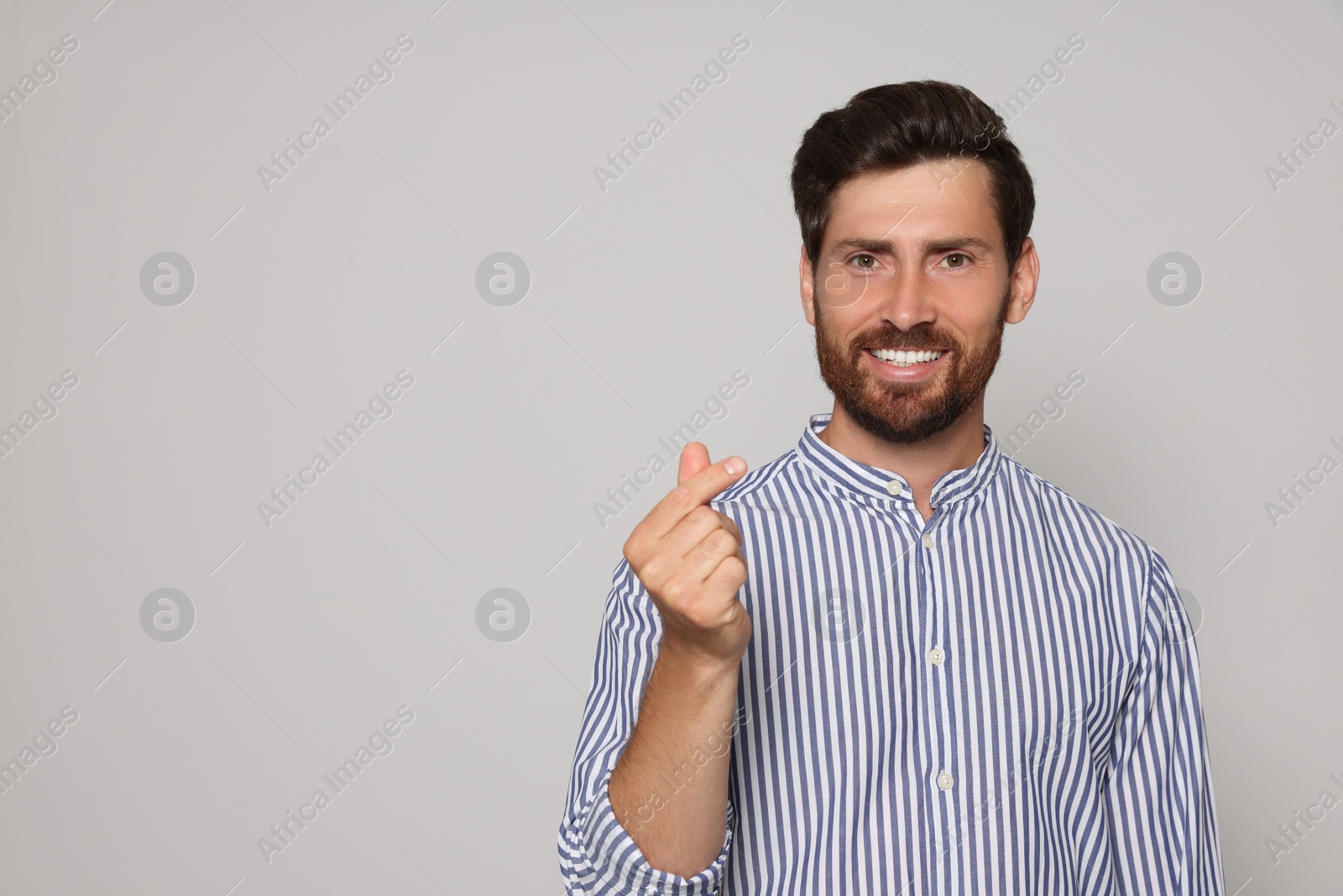 Photo of Handsome bearded man showing heart gesture on light grey background. Space for text