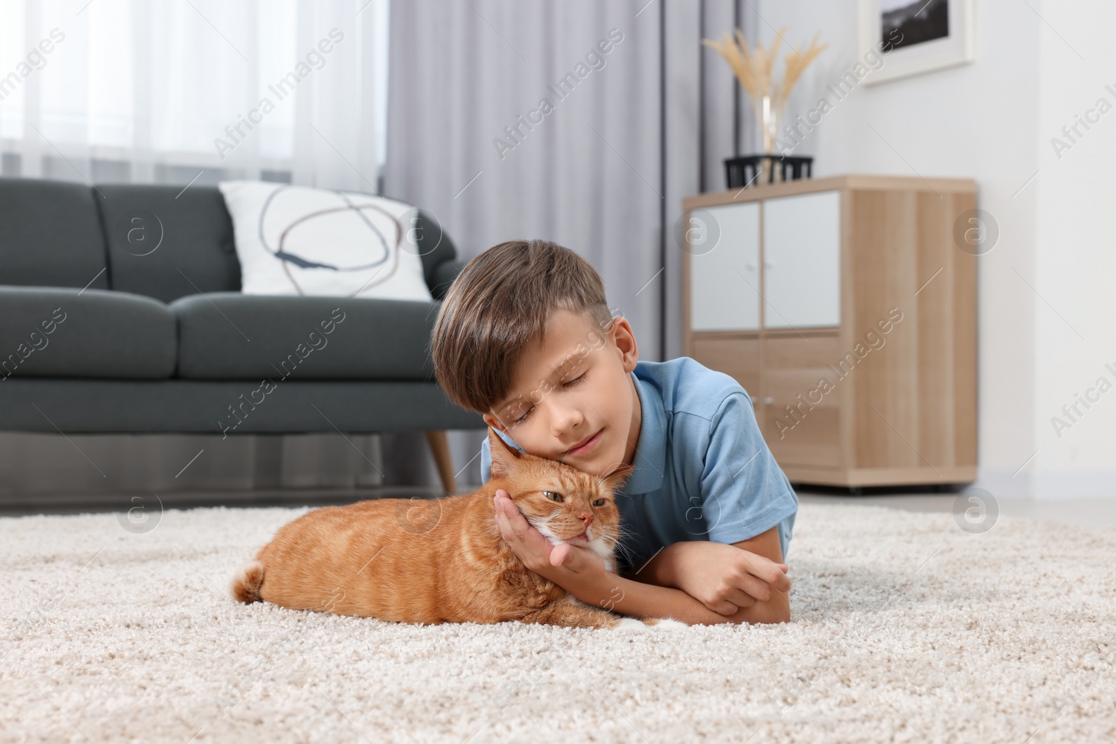 Photo of Little boy with cute ginger cat on soft carpet at home