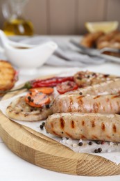 Photo of Tasty grilled sausages with vegetables and spices on white wooden table, closeup