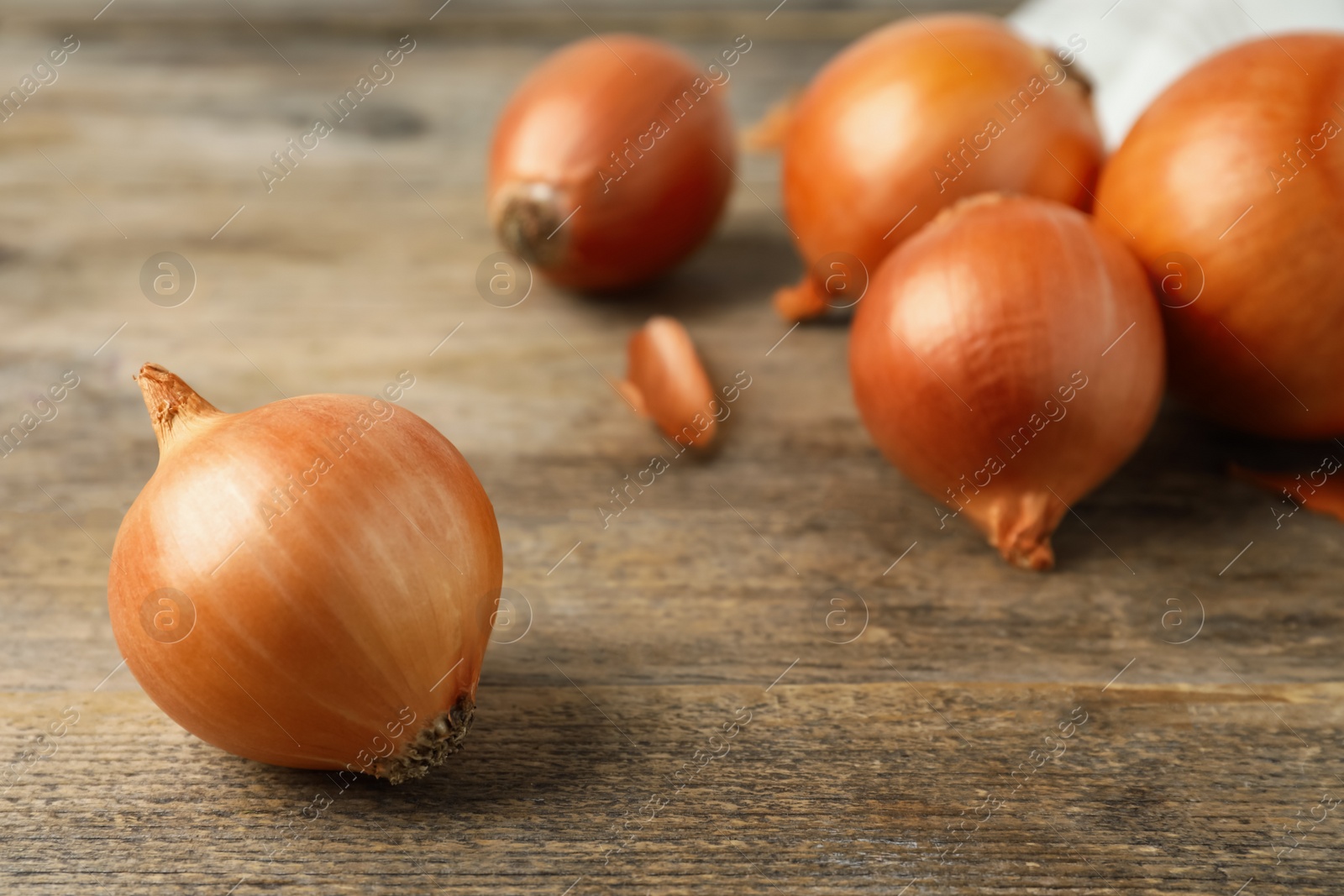 Photo of Ripe yellow onion bulbs on wooden table, closeup