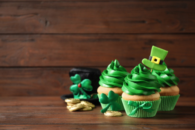 Photo of Decorated cupcakes and coins on wooden table, space for text. St. Patrick's Day celebration