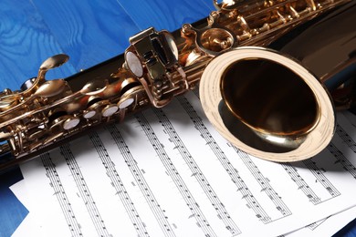 Photo of Beautiful saxophone and note sheets on blue wooden background, closeup