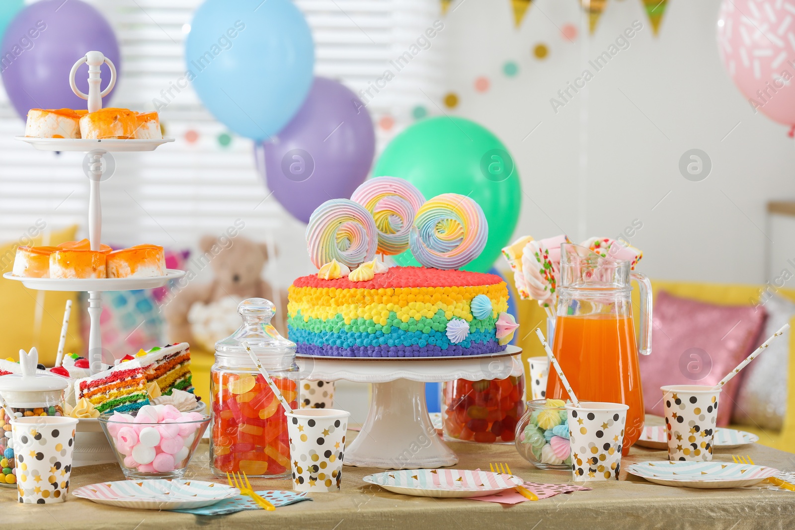 Photo of Bright birthday cake and other treats on table in decorated room