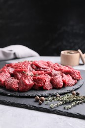 Photo of Pieces of raw beef meat, peppercorns and thyme sprigs on grey textured table