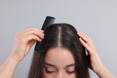 Photo of Woman with comb examining her hair and scalp on grey background, closeup. Dandruff problem