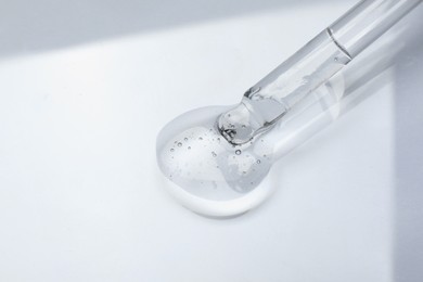 Photo of Dripping cosmetic oil from pipette onto light surface, closeup