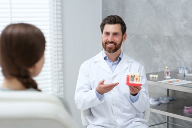 Doctor with educational model of dental implant consulting patient in clinic