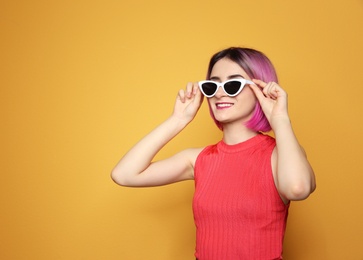 Photo of Young woman with trendy hairstyle wearing sunglasses against color background