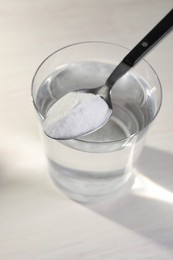 Photo of Glass of water and spoon with baking soda on light background