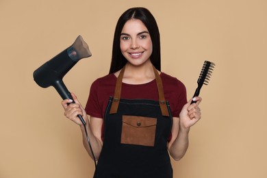 Portrait of happy hairdresser with hairdryer and vent brush on beige background