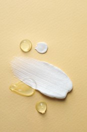 Photo of Samples of transparent gel and white cream on yellow background, flat lay