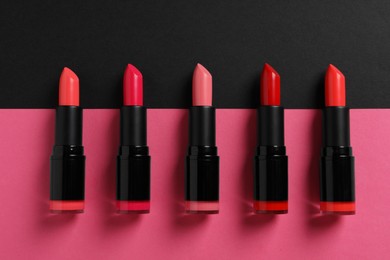 Photo of Beautiful lipsticks on black and pink background, flat lay