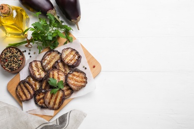 Photo of Delicious grilled eggplant slices with parsley and spices on white wooden table, flat lay. Space for text