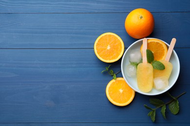 Photo of Tasty orange ice pops and space for text on blue wooden table, flat lay. Fruit popsicle