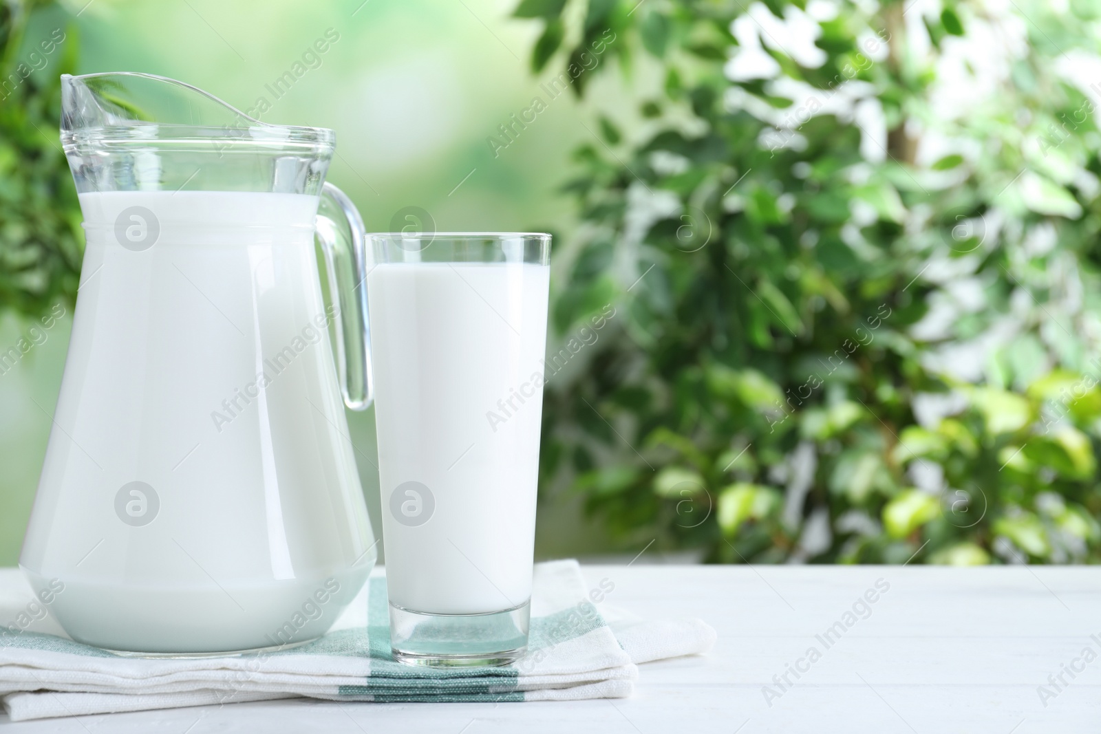 Photo of Jug and glass with fresh milk on white wooden table against blurred background. Space for text