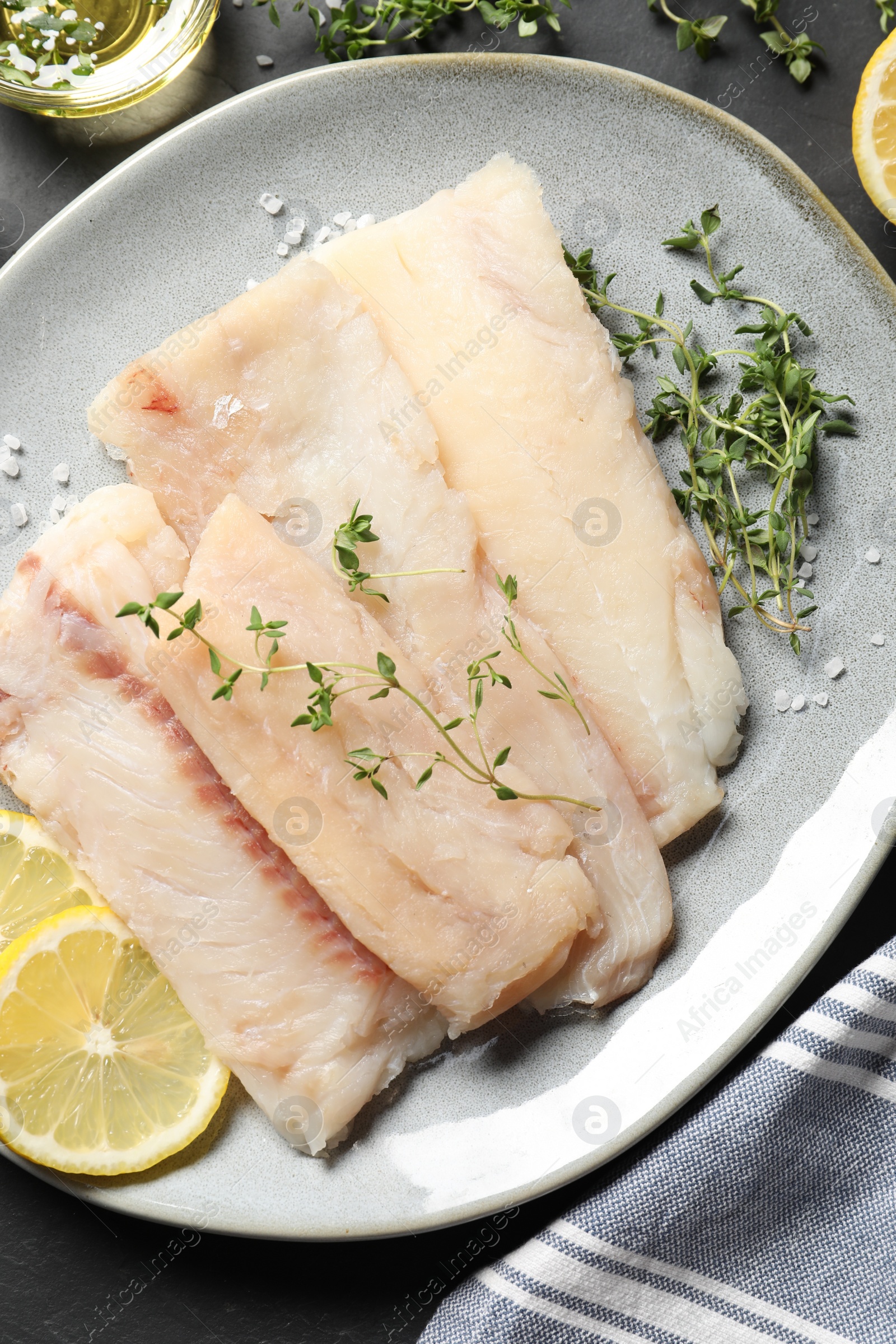 Photo of Plate with raw cod fish, microgreens, lemon and salt on dark table, top view