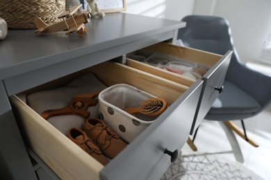 Photo of Open cabinet drawer with baby shoes and accessories in child room