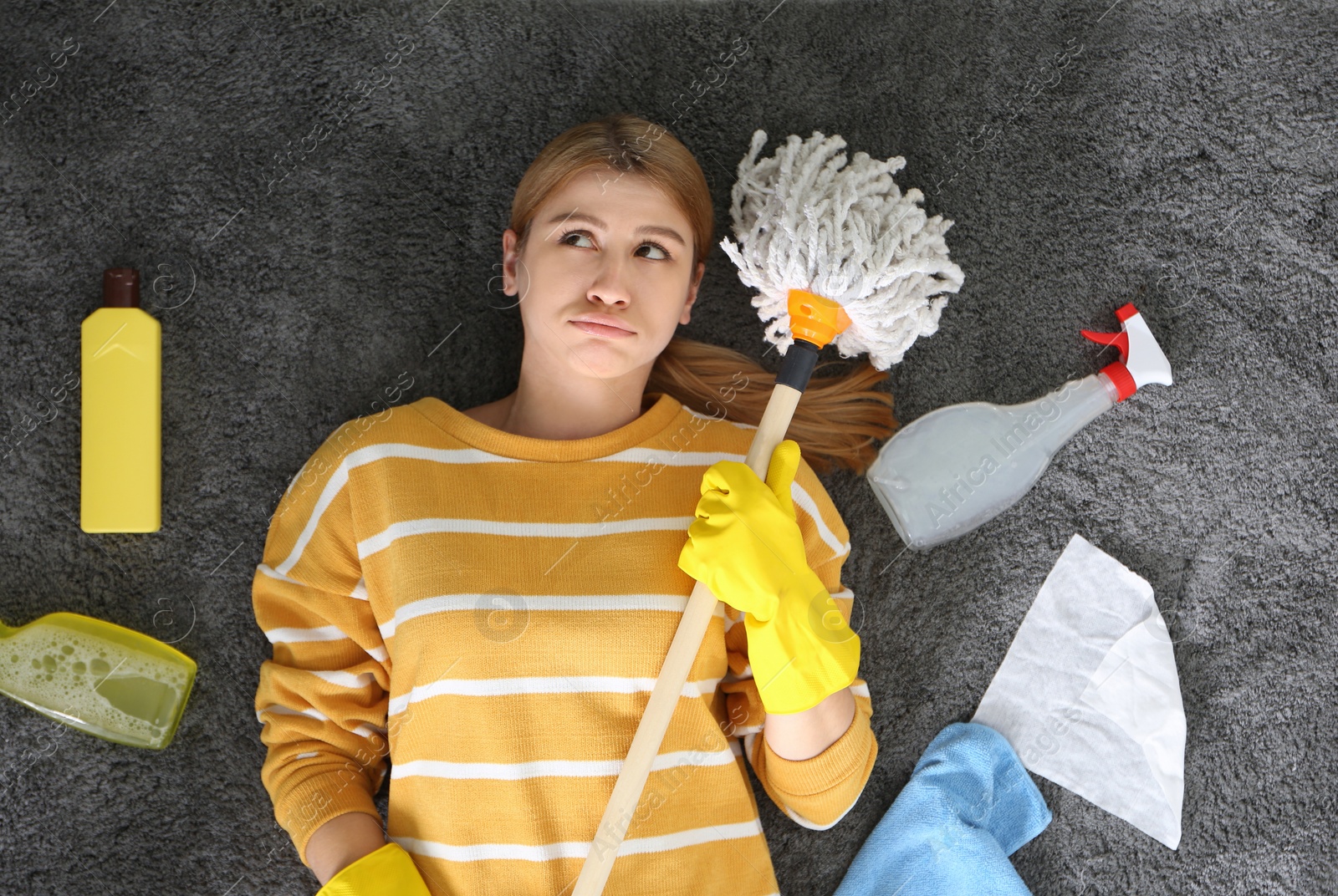 Photo of Lazy young woman with cleaning equipment lying on floor at home, top view