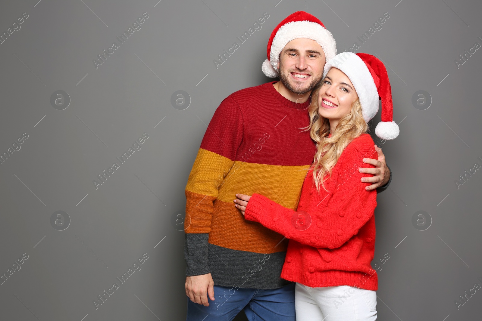 Photo of Young couple in Santa hats on grey background. Christmas celebration