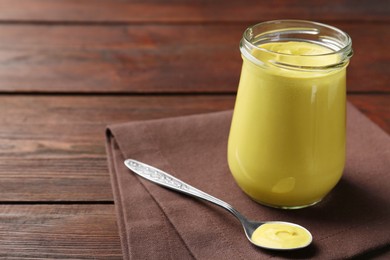 Photo of Glass jar and spoon with tasty mustard sauce on wooden table, space for text