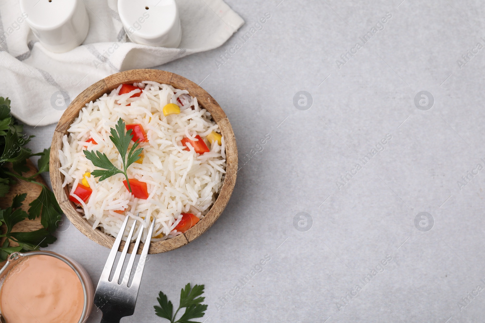 Photo of Bowl of delicious rice with vegetables and parsley served on light gray table, flat lay. Space for text