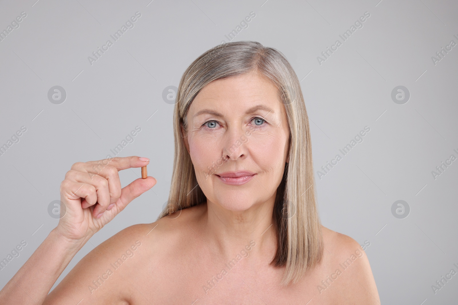 Photo of Beautiful woman with vitamin capsule on grey background