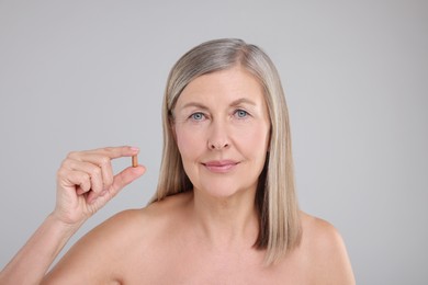 Beautiful woman with vitamin capsule on grey background