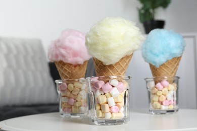 Photo of Sweet cotton candies in waffle cones and marshmallows on white table indoors, closeup