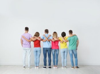 Photo of Group of young people hugging each other near light wall. Unity concept