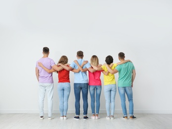 Group of young people hugging each other near light wall. Unity concept